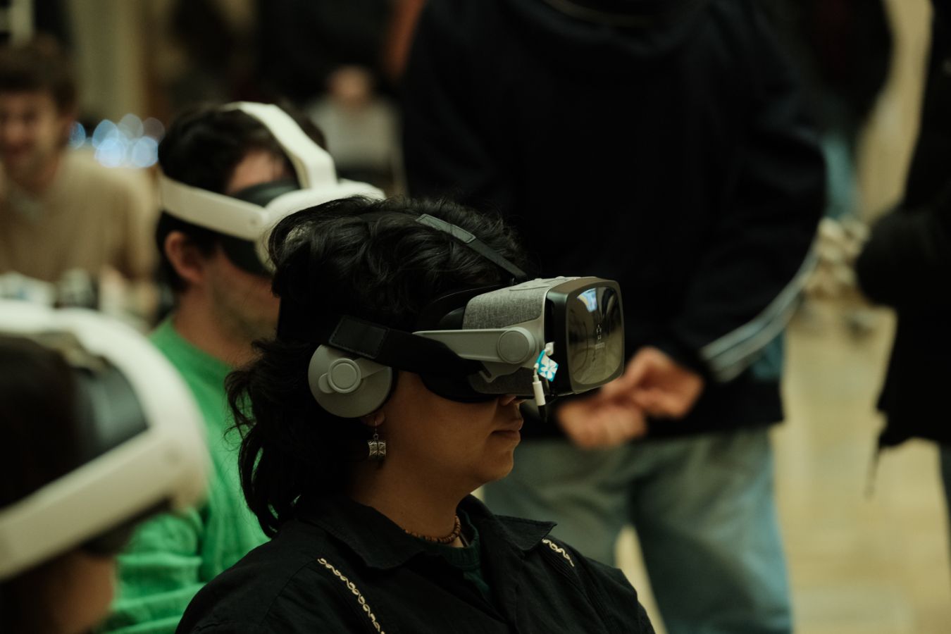 VR-Simulation: Nahaufnahme einer Person mit Virtual-Reality-Brille und Kopfhörern, sitzend in einer belebten Ausstellungshalle.